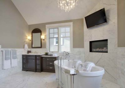 White soaker bathtub placed next to built in fireplace and large tv