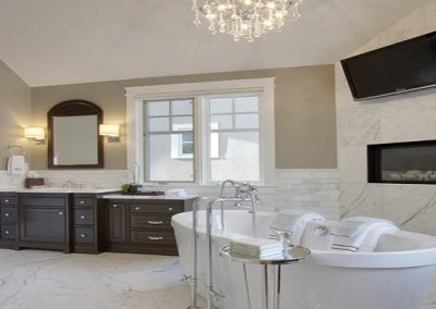 White soaker bathtub placed next to built in fireplace and large tv