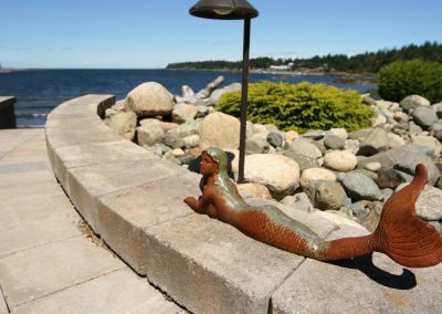 Rustic mermaid statue surrounded by landscaped area in oceanfront backyard